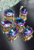 Purple Aqua AB pear-shaped 2 hole slider bead in a gold setting featuring a faceted rhinestone with vibrant purple, aqua blue, teal, and turquoise flashes. This decorative focal bead is designed for bracelet making, necklace designs, bead weaving, and handmade jewelry projects. The teardrop shape and sparkling finish create an elegant centerpiece for custom jewelry creations.