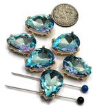 Six Aquamarine pear-shaped 2 Hole Slider Beads with faceted rhinestones in polished gold settings displayed on a white background beside a dime and beading needles for size reference. The sparkling rhinestones feature aquamarine blue tones with flashes of violet, lavender, pink, and turquoise. These dual-hole teardrop beads are ideal focal components for handmade bracelets, necklaces, earrings, pendants, bead weaving projects, and custom jewelry designs.