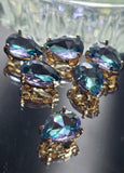 Close-up view of faceted Aquamarine rhinestone 2 Hole Slider Beads featuring polished gold settings and brilliant sparkle. The pear-shaped stones showcase vibrant blue tones with flashes of violet, pink, lavender, and turquoise visible throughout the faceted design. Their dual-hole construction helps keep jewelry strands aligned, making these slider beads ideal for multi-strand bracelets, necklaces, bead weaving projects, and decorative handmade accessories.
