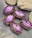 Detailed view of marquise 2 Hole Slider Beads with faceted violet center stones and coordinating light amethyst rhinestones around the perimeter. The polished silver-tone settings provide a sophisticated finish. A dime and beading pin illustrate size and stringing possibilities. These jewelry making supplies are suitable for creating custom bracelets, layered necklaces, decorative pendants, earrings, and unique handcrafted jewelry designs with beautiful purple sparkle.