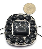 Oversized western focal bead with a black faux marble center stone accented by a decorative border of oval stones and antique silver detailing. A dime is included for scale, highlighting the substantial size of this slider bead. The dual-hole construction makes it suitable for multi-strand bracelets, necklaces, pendants, leather jewelry, artisan jewelry, and handcrafted western-inspired jewelry designs requiring a bold centerpiece.