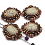 Western-style 2 Hole Slider Beads featuring oval faux marble stones with ivory and cream veining set in ornate antique copper settings. Decorative rope details and raised bead accents surround each center stone. Displayed with beading pins showing the dual-hole construction, these focal beads are ideal for handmade bracelets, western necklaces, leather jewelry, artisan accessories, and Southwestern-inspired jewelry making projects.