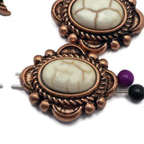 Antique copper slider beads with ivory faux marble stones arranged for jewelry making photography. Decorative scrollwork, rope detailing, and raised accents surround the oval center stones, creating a bold western focal design. The dual-hole construction supports multi-strand jewelry projects. Ideal for western bracelets, necklaces, leather accessories, custom jewelry collections, and Southwestern-inspired handmade creations.