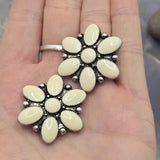 Decorative flower-shaped 2 Hole Slider Beads featuring cream enamel coloring and antique silver settings. The floral design creates an eye-catching focal point suitable for many jewelry styles. Photographed on a gray background with decorative stones, these beads are perfect for bracelets, necklaces, pendants, artisan beadwork, and feminine handmade jewelry collections.