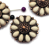 Flower-shaped focal beads with soft cream-colored faux stone accents and warm antique copper detailing. The decorative western design combines floral elegance with rustic styling. Photographed with a dime for size reference and beading pins showing the dual-hole construction, these beads are ideal for bracelets, necklaces, artisan jewelry, leather projects, and handcrafted accessories.