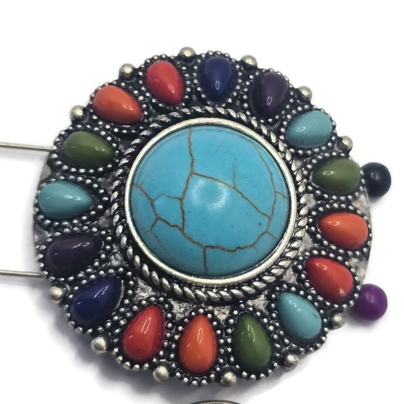 Oversized western-style 2 Hole Slider Bead featuring a large faux turquoise center stone surrounded by colorful faux stone accents in orange, green, blue, purple, and turquoise tones. Set in antique silver metal, this statement focal bead is displayed on a hand to demonstrate scale. Perfect for handmade bracelets, western necklaces, artisan jewelry, Southwestern accessories, and custom jewelry making projects.