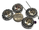 Round Tree of Life 2 Hole Slider Beads featuring raised tree designs in mixed antique copper and light antique gold finishes set against antique silver backgrounds. Displayed on a hand for size reference, these symbolic focal beads are perfect for handmade bracelets, necklaces, inspirational jewelry, family-themed accessories, artisan beadwork, and meaningful jewelry making projects.