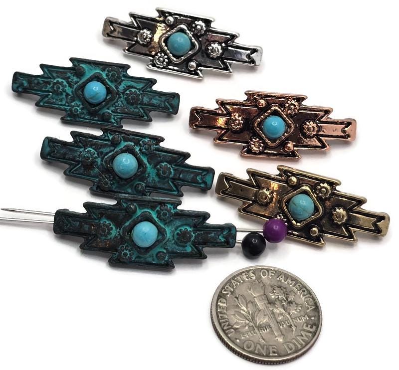 Southwestern-style 2 Hole Slider Beads featuring faux turquoise center stones set in mixed finishes including antique silver, antique copper, antique brass, and verdigris patina. The geometric focal beads display bold tribal-inspired patterns with decorative floral accents and raised metal details. A dime and beading pins are included for size reference. Perfect for handmade bracelets, western necklaces, artisan jewelry, leather projects, and Southwestern-inspired jewelry making designs.