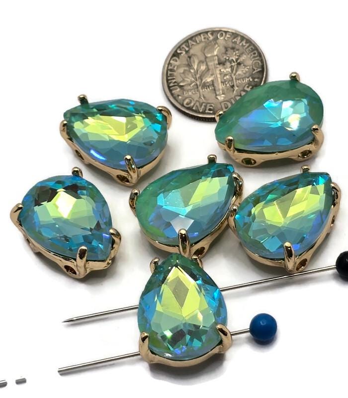 Sparkling Seafoam Green AB 2 Hole Slider Beads featuring faceted pear-shaped rhinestones in polished gold settings. The Aurora Borealis coating creates vibrant color shifts from seafoam green to turquoise, aqua blue, and lime tones. Displayed on a white background with a dime and jewelry needles for size reference, these dual-hole beads are ideal for bracelet making, necklace designs, bead weaving, pendants, and custom handmade jewelry creations.
