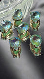 Seafoam Green AB pear-shaped 2 Hole Slider Beads with faceted rhinestones and polished gold settings arranged around a dime for size reference. The Aurora Borealis finish creates dazzling flashes of turquoise, aqua blue, lime green, and seafoam tones. These dual-hole slider beads feature a teardrop shape that works beautifully as a focal element in bracelets, necklaces, earrings, bead weaving projects, and custom handmade jewelry designs.