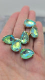 Faceted Seafoam Green AB rhinestone 2 Hole Slider Beads in polished gold settings shown with a dime and beading needles for scale. The teardrop-shaped beads feature two parallel holes for secure stringing and balanced jewelry designs. Their shimmering Aurora Borealis finish displays beautiful seafoam green, turquoise, aqua blue, and lime reflections, making them perfect focal beads for handmade bracelets, necklaces, earrings, and decorative accessories.