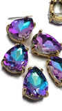 Close-up view of Purple Aqua AB rhinestone slider beads with gold settings and two parallel stringing holes. These faceted pear-shaped beads display shifting shades of purple, aqua, turquoise, and teal as they reflect light. Ideal for creating bracelets, necklaces, earrings, pendants, bead weaving projects, and unique handmade jewelry designs.