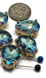 Faceted Aquamarine 2 Hole Slider Beads with polished gold settings shown grouped together on a reflective background. The rhinestones display brilliant blue color with hints of lavender, violet, pink, and turquoise that appear as light moves across the surface. These dual-hole teardrop beads make beautiful focal pieces for bracelets, necklaces, earrings, keychains, bead embroidery, and custom jewelry creations.