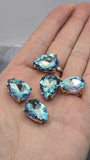 Six faceted Aquamarine rhinestone slider beads arranged on a glossy black reflective surface. The teardrop-shaped stones feature brilliant blue coloring with shimmering flashes of lavender, violet, pink, and turquoise throughout the faceted design. Set in polished gold settings with dual stringing holes, these 2 Hole Slider Beads are ideal for bracelets, necklaces, earrings, pendants, and custom jewelry making projects.
