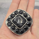 Western-style focal bead showcasing faux marble detailing and antique silver accents. The oversized center stone features realistic white veining against a black background, surrounded by matching oval stones. Displayed beside a dime for scale, this dual-hole slider bead is designed for bracelet making, necklace designs, leather cord projects, artisan jewelry, and bold handmade accessories with Southwestern-inspired style.