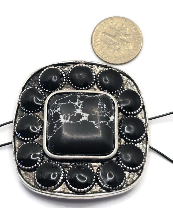 Large western-style 2 Hole Slider Bead featuring a square faux marble center stone with white veining surrounded by oval black stones in an antique silver setting. Displayed beside a dime for size reference, this oversized focal bead includes dual holes for multi-strand jewelry construction. Ideal for handmade bracelets, western necklaces, statement jewelry, leather jewelry designs, custom accessories, and Southwestern-inspired jewelry making projects.