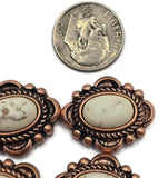 Antique copper focal beads with oval faux marble center stones displaying soft cream coloring and natural-looking veining. The decorative western setting features detailed metalwork and raised accents that create a rustic handcrafted appearance. Beading pins demonstrate the dual-hole design used for multi-strand jewelry. Perfect for bracelets, necklaces, leather jewelry, beadwork projects, and western-inspired handmade accessories.