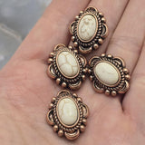 Large western-style slider beads with ivory faux marble center stones and ornate antique copper settings. The detailed metalwork creates texture and visual interest while the neutral stone color complements many jewelry styles. Displayed with beading pins showing the stringing holes, these 2 Hole Slider Beads are ideal for bracelets, necklaces, leather projects, custom jewelry, and handcrafted accessories.