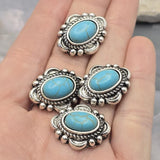 Beautiful faux turquoise focal beads framed by ornate antique silver metalwork with rope detailing and raised accents. The vibrant blue-green stones display realistic veining that creates a classic western appearance. A dime provides size comparison while beading pins demonstrate the dual-hole design. Ideal for bracelet making, necklace designs, leather jewelry, and handcrafted Southwestern-style accessories.