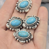 Western focal beads with vibrant faux turquoise stones accented by detailed antique silver settings. The oval center stones feature natural-looking veining and are surrounded by textured rope borders and raised bead details. Shown with a dime and beading pins for reference, these slider beads are excellent for handmade bracelets, necklaces, leather projects, and Southwestern-inspired jewelry designs.