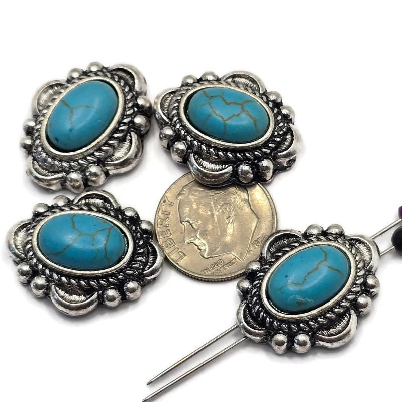 Western-style 2 Hole Slider Beads featuring oval faux turquoise stones with natural-looking matrix veining set in detailed antique silver settings. Displayed with a dime for size reference and beading pins showing the dual-hole construction, these focal beads are perfect for handmade bracelets, western necklaces, leather jewelry, Southwestern accessories, and artisan jewelry making projects.