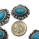 Antique silver western slider beads featuring vibrant faux turquoise center stones and decorative rope detailing throughout the setting. The blue-green stones create a bold focal point while the dual-hole construction supports balanced jewelry designs. Photographed with a dime and beading pins, these beads are ideal for bracelets, necklaces, leather accessories, and custom jewelry projects