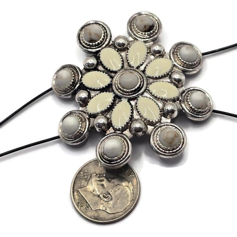 Large western-style 2 Hole Slider Bead featuring cream and white enamel accents arranged in a floral starburst pattern within an antique silver setting. Displayed with a dime for size reference, this oversized focal bead includes dual holes for multi-strand jewelry designs. Perfect for handmade bracelets, western necklaces, statement jewelry, leather accessories, artisan beadwork, and Southwestern-inspired jewelry making projects.