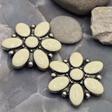 Beautiful floral slider beads with cream enamel petals and antique silver detailing. The flower design features six elongated enamel petals surrounding a coordinating center accent. Shown on a decorative background with stones, these 2 Hole Slider Beads are ideal for bracelet making, necklace designs, artisan jewelry, bridal accessories, and handcrafted floral-themed jewelry projects.