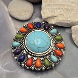 Large western focal bead featuring a turquoise-look center stone and a ring of colorful faux stone accents in blue, purple, orange, and green. The antique silver finish provides contrast and vintage-inspired detail throughout the design. This statement slider bead is ideal for handmade jewelry, leather projects, bracelets, necklaces, beadwork, and artisan accessory collections.