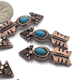 Antique copper arrow slider beads featuring faux turquoise accents and decorative western styling. The dual-hole construction supports multi-strand jewelry designs while the arrow shape creates a meaningful focal point. Displayed beside a dime for size reference, these beads are excellent for handmade jewelry, western accessories, artisan beadwork, and custom fashion designs.