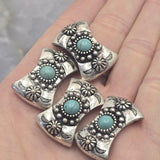 Curved western focal beads with faux turquoise center stones and detailed antique silver metalwork. Decorative bead accents, floral elements, and crescent details create a classic Southwestern appearance. Displayed on a hand to demonstrate scale, these slider beads work beautifully in bracelet making, necklace designs, artisan jewelry, leather accessories, and handcrafted western-inspired creations.