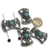Western-style 2 Hole Slider Beads featuring faux turquoise center stones surrounded by decorative silver beadwork and floral accents in antique silver settings. Displayed on a gray background with decorative stones, these curved focal beads are ideal for handmade bracelets, western necklaces, leather jewelry, artisan accessories, Southwestern jewelry designs, and custom jewelry making projects.