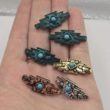 Western-inspired 2 Hole Slider Beads featuring turquoise-look center stones framed by decorative metalwork in assorted finishes. The bold geometric shape combines tribal styling with rustic details, while the mixed metal finishes add variety and visual interest. Displayed with beading pins and a dime for reference, these focal beads work beautifully in handmade bracelets, necklaces, artisan jewelry, leather projects, and custom jewelry creations.