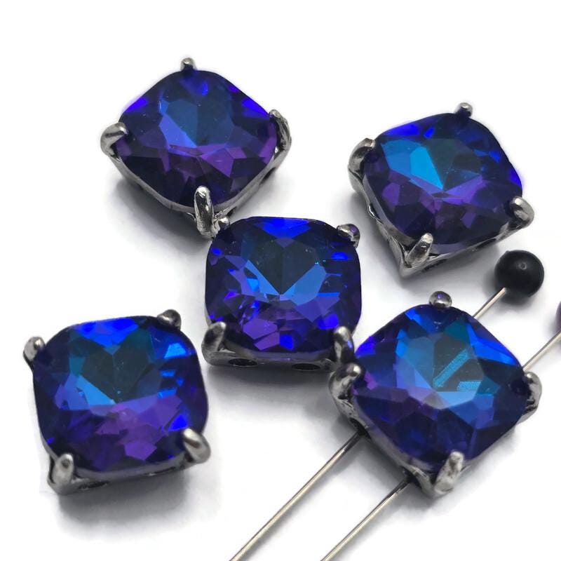 Create stunning handmade jewelry with these Royal Blue and Amethyst Slider Beads. The faceted glass stones reflect beautiful flashes of deep blue and violet while the gun metal finish enhances their rich coloring. Ideal for bracelet making, necklace designs, pendants, and artisan jewelry, these focal beads provide exceptional visual impact. Their two-hole construction offers versatility for bead weaving, loom work, and multi-strand jewelry projects.