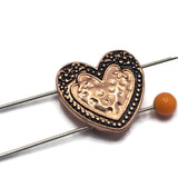 Featuring a raised heart surrounded by detailed scrollwork and beaded accents, these Heart Slider Beads bring timeless beauty to handmade jewelry. The bright copper finish with antique detailing complements natural stone beads, turquoise, crystals, pearls, and leather cord. Perfect for bracelets, necklaces, pendants, and artisan jewelry, these decorative focal beads provide both symbolism and functionality through their durable two-hole design.