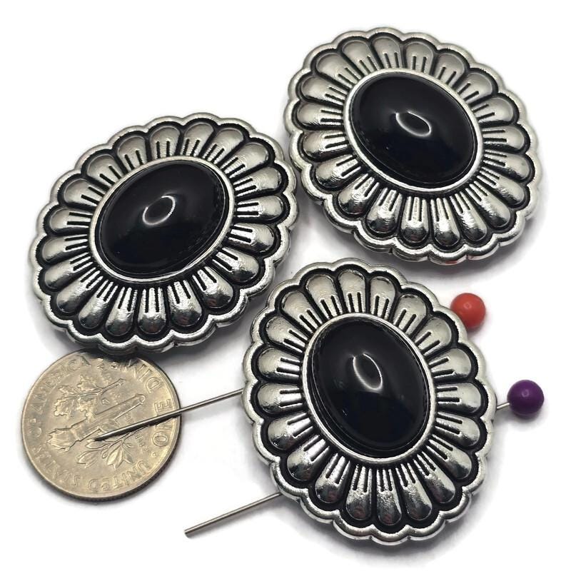 These Western Concho 2 Hole Slider Beads feature a smooth jet black lucite center framed by platinum silver with antique detailing. The classic scalloped concho design makes these focal beads perfect for bracelet making, necklace designs, earrings, and pendants. Their dual-hole construction provides excellent alignment for multi-strand jewelry while adding timeless Western style to handmade jewelry, leather accessories, and artisan jewelry creations.