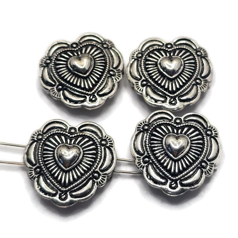 These antique silver Heart Concho Style 2 Hole Slider Beads bring Western charm and timeless symbolism to handmade jewelry designs. Featuring a raised heart center surrounded by detailed sunburst accents and decorative metalwork, they create beautiful focal points for bracelets, necklaces, and earrings. The dual-hole construction makes them ideal for multi-strand jewelry, bead weaving, leather jewelry, and artisan jewelry projects that celebrate love, friendship, and meaningful connections.