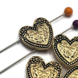These heart-shaped 2 Hole Slider Beads combine a bright gold finish with antique detailing to create an elegant focal bead for handmade jewelry. The textured heart centerpiece and decorative border add depth and visual interest while coordinating beautifully with leather cord, crystals, pearls, seed beads, and natural stones. Perfect for bracelets, necklaces, pendants, and multi-strand jewelry projects of every style.
