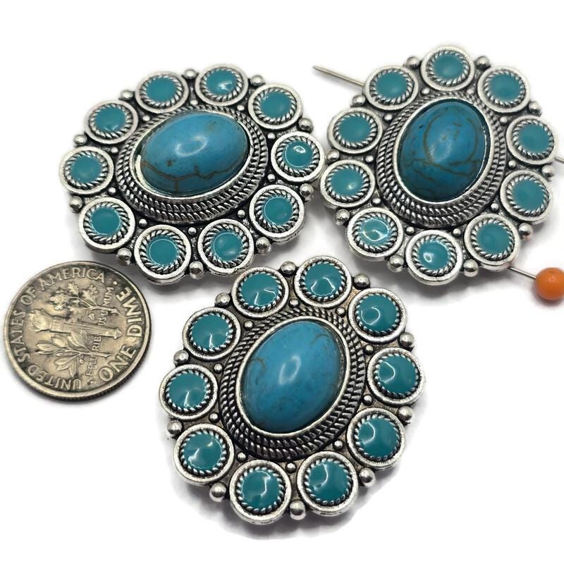 Create beautiful Western-inspired jewelry with these Silver Turquoise 2 Hole Slider Beads. Featuring a large faux turquoise center stone surrounded by smaller turquoise accents in an ornate silver concho setting, these focal beads are perfect for bracelets, necklaces, and multi-strand jewelry. Pair them with leather, natural stone beads, or silver findings to create rustic, Southwestern, rodeo, and boho jewelry with timeless Western charm.