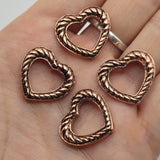 Add warm antique copper color to handmade jewelry with these open heart 2 hole slider beads. A dimensional twisted rope pattern surrounds the heart while dark antiqued detailing highlights the textured design. Hidden back loops make these focal beads perfect for double strand bracelets and creative bead weaving. Keep the heart center completely open or decorate visible strands with seed beads for a customized look. Great jewelry making supplies for bracelets and necklaces.