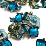 Ornate floral 2 hole slider beads featuring faceted Blue Zircon crystals, pale blue enamel flowers, teal leaves, and a warm antique gold finish. These decorative jewelry making beads create beautiful focal points for double strand bracelets, necklaces, bead weaving, and seed bead designs. Perfect for bohemian jewelry, botanical accessories, garden-inspired jewelry, and colorful handmade designs.