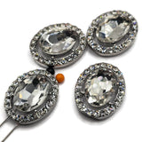 Large clear rhinestone 2 hole slider beads featuring a brilliant faceted glass center stone surrounded by sparkling clear crystal rhinestones in a platinum silver metal tone setting. These elegant oval focal beads are perfect for bridal jewelry, wedding bracelets, statement necklaces, double strand bracelets, bead weaving, and handmade jewelry designs. Beautiful jewelry making supplies for creating glamorous crystal jewelry with exceptional sparkle and a polished boutique-quality appearance.