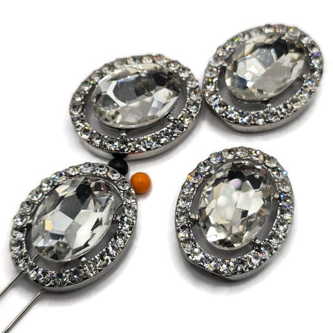 Large clear rhinestone 2 hole slider beads featuring a brilliant faceted glass center stone surrounded by sparkling clear crystal rhinestones in a platinum silver metal tone setting. These elegant oval focal beads are perfect for bridal jewelry, wedding bracelets, statement necklaces, double strand bracelets, bead weaving, and handmade jewelry designs. Beautiful jewelry making supplies for creating glamorous crystal jewelry with exceptional sparkle and a polished boutique-quality appearance.
