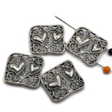 Filigree heart slider beads in platinum silver tone featuring intricate scroll patterns and two dimensional heart accents. These 2 hole focal beads work beautifully for double strand bracelets, bead weaving, necklaces, seed bead jewelry, DIY bracelets, and romantic handmade jewelry designs.