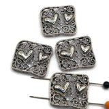 Openwork platinum silver heart beads with ornate filigree detailing for jewelry making. These 2 hole slider beads feature raised hearts and scrolling metalwork, making them beautiful focal beads for bracelets, necklaces, bead weaving, seed bead designs, multi-strand jewelry, and DIY jewelry projects.