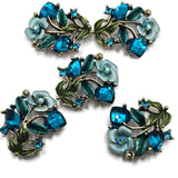 Antique gold floral 2 hole slider beads featuring brilliant Blue Zircon rhinestones, soft blue enamel flowers, and teal green enamel leaves. These botanical focal beads are perfect for double strand bracelets, necklaces, bead weaving, seed bead jewelry, and handmade jewelry designs. Dimensional flowers, vines, and sparkling crystals create an ornate vintage-inspired look.