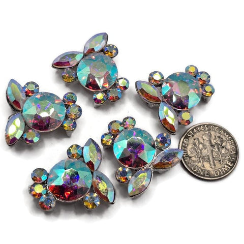 Clear AB rhinestone 2 hole slider beads featuring a large faceted round crystal surrounded by marquise and smaller round rhinestones. These platinum silver focal beads reflect brilliant flashes of aqua, pink, purple, green, gold, and blue. Perfect for double strand bracelets, bead weaving, necklaces, seed bead jewelry, bridal designs, and DIY jewelry making, these sparkling Aurora Borealis beads add incredible color and dimension to handmade jewelry.