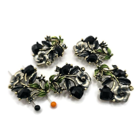 Antique gold floral 2 hole slider beads feature faceted jet black rhinestones, green and gray enamel accents, and beautifully detailed dimensional flowers and leaves. These dramatic focal beads are perfect for bracelets, necklaces, bead weaving, and multi-strand jewelry designs. The two-hole construction helps keep strands aligned while adding a professional finished look. Each bead measures approximately 30 mm x 21 mm with 12 mm between the loops. Five beads per package.