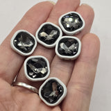 White enamel 2-hole slider beads with faceted black diamond rhinestone centers for bracelet and jewelry making. Each square metal focal bead features a smoky gray crystal-style stone that catches the light with multiple reflective facets. Two stringing holes on each side make these slider beads useful for double-strand bracelets, bead weaving, necklaces, and creative jewelry designs. Statement jewelry components for handmade bracelets, beading projects, and jewelry making at home.