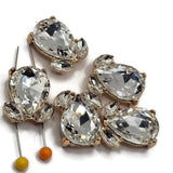 Sparkling Clear rhinestone 2 hole focal beads featuring a warm bright gold metal setting for handmade jewelry designs. Each statement slider bead measures approximately 20 mm by 16 mm and features one large faceted teardrop crystal with two smaller rhinestone accents. Hidden stringing loops make these decorative components beautiful for beaded bracelets, necklaces, bead weaving, bridal jewelry, and multi-strand designs.
